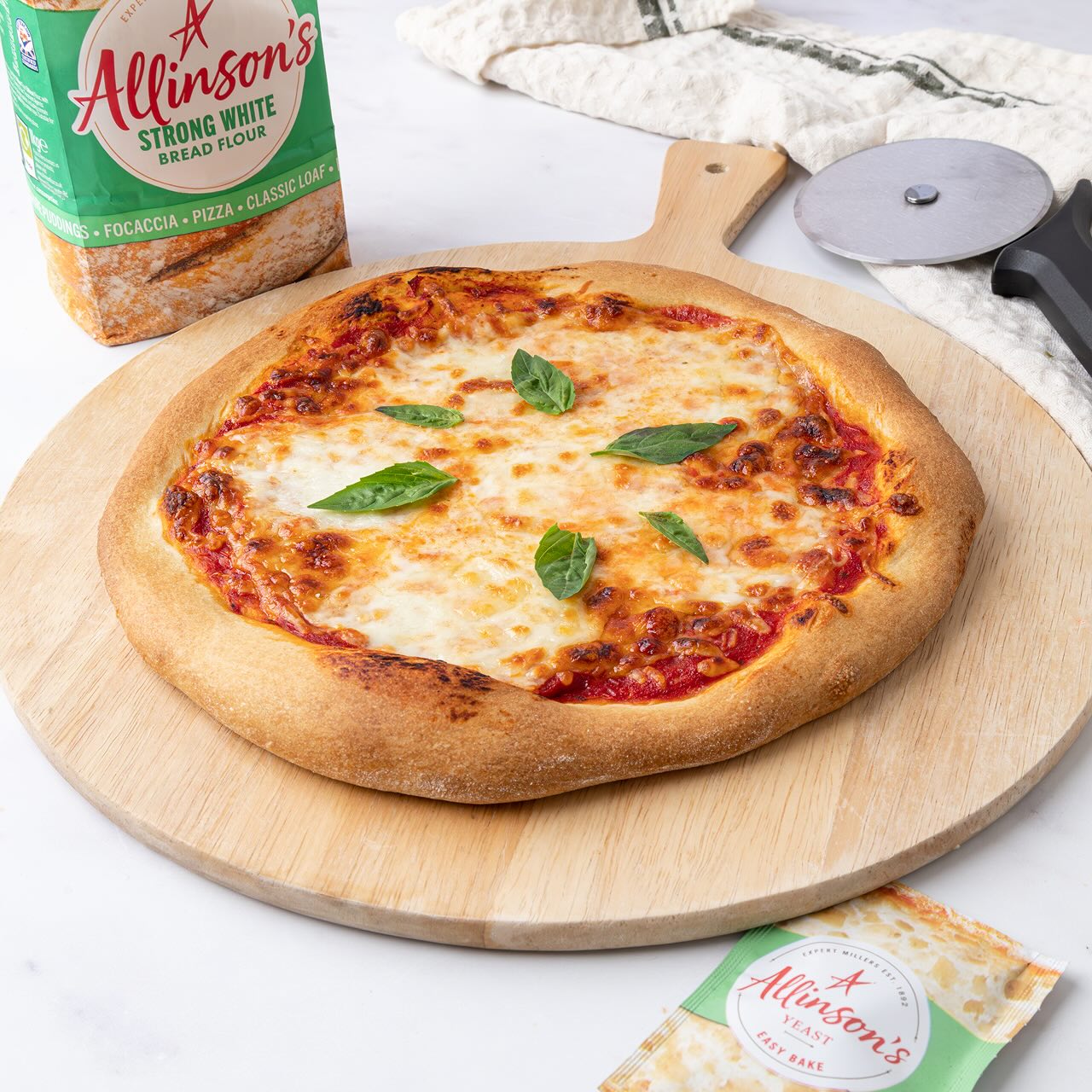 A home made pizza sits on a table, alongside a pack of Allinson's Strong White Bread Flour and Allinson's Yeast.